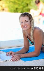 Young blonde woman using a laptop by the swimming pool