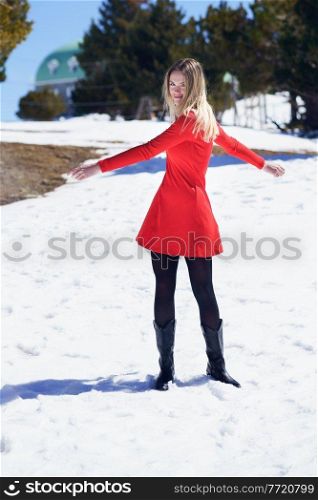 Young blonde woman wearing a red dress and black stockings opening her arms in happiness in the snowy mountains, in Sierra Nevada, Granada, Spain.. Woman wearing a red dress and black stockings opening her arms in happiness in the snowy mountains.