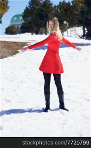 Young blonde woman wearing a red dress and black stockings opening her arms in happiness in the snowy mountains, in Sierra Nevada, Granada, Spain.. Woman wearing a red dress and black stockings opening her arms in happiness in the snowy mountains.