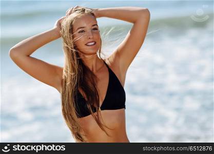 Young blonde woman with beautiful body in swimwear on a tropical. Young blonde woman with beautiful body in swimwear on a tropical beach. Caucasian female with straight long hairstyle wearing black bikini.