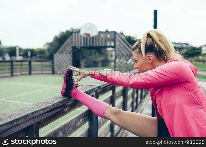 Young blonde woman with pigtail stretching her legs before training outdoors. Young woman stretching legs before training outdoors