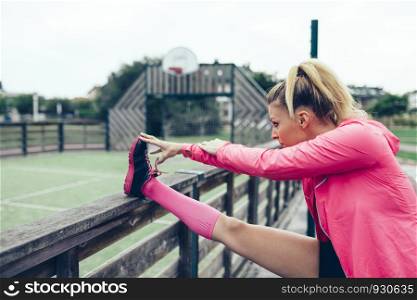 Young blonde woman with pigtail stretching her legs before training outdoors. Young woman stretching legs before training outdoors