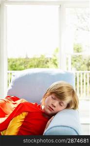 Young boy (7-9) sleeping in armchair wearing superhero costume indoors
