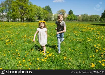 Young boy and girl brither and sister running in a sunny meadow with dandelion flowers family fun concept. Children running in sunny meadow
