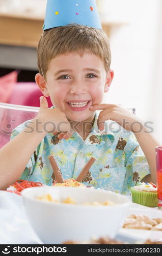 Young boy at party sitting at table with food smiling