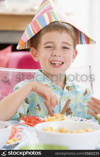 Young boy at party sitting at table with food smiling