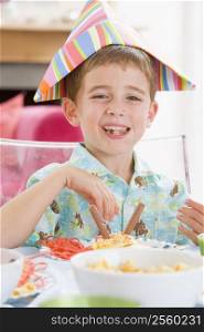 Young boy at party sitting at table with food smiling