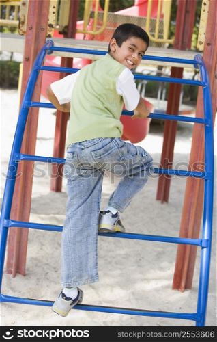 Young boy climbing on playground structure smiling (selective focus)