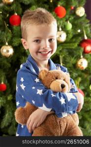 Young Boy Cuddling Teddy Bear In Front Of Christmas Tree