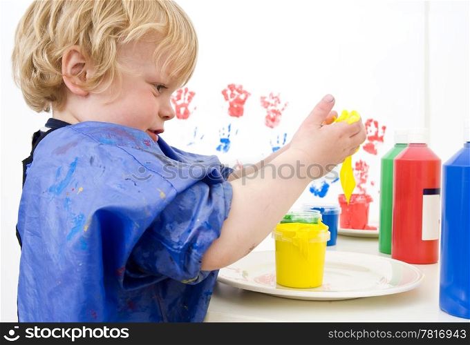 Young boy dipping his hands in a pot of finger paint