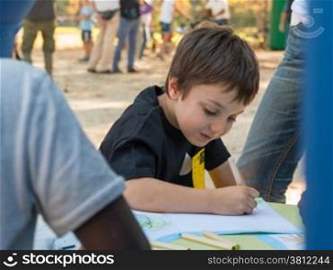 young boy drawing on a paper with colorful pencil in a park