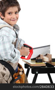 Young boy dressed as an adult carpenter cutting wood with a saw