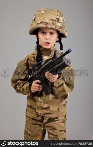 Young boy dressed like a soldier with rifle isolated on gray background