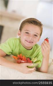 Young boy eating bowl of vegetables in living room smiling