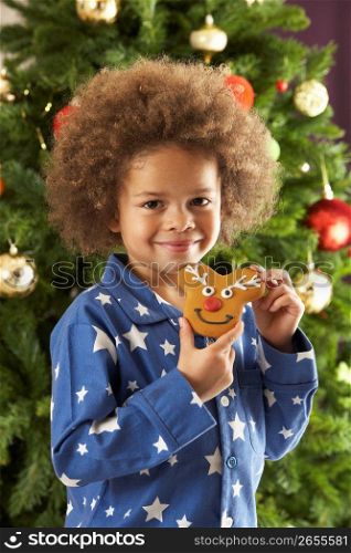 Young Boy Eating Cookie In Front Of Christmas Tree