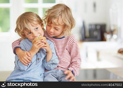 Young boy eating muffin while his brother looks on