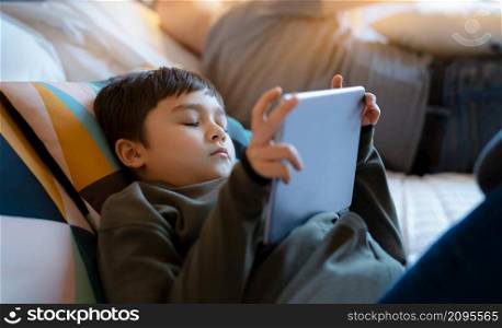 Young boy falling sleep while watching cartoon on tablet, Tried kid lying in bed play game online, Child sleeping while reading e-book on digital tablet, School boy relaxing at home