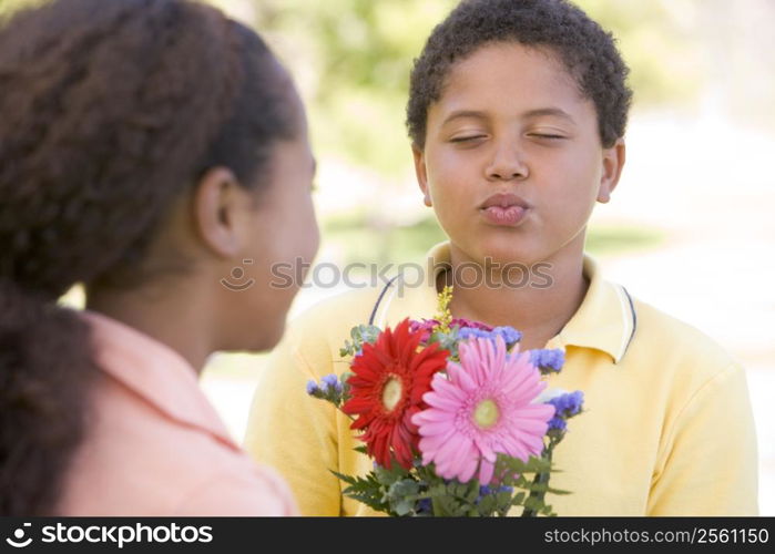 Young boy giving young girl flowers and puckering up