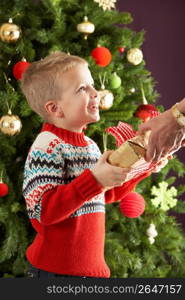 Young Boy Holding Christmas Present In Front Of Christmas Tree