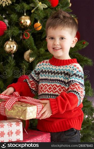 Young Boy Holding Christmas Present In Front Of Christmas Tree