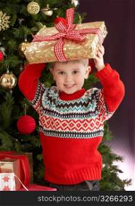 Young Boy Holding Christmas Present In Front Of Christmas Tree