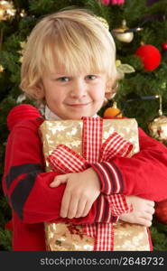 Young Boy Holding Gift In Front Of Christmas Tree