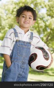 Young boy holding soccer ball outdoors smiling
