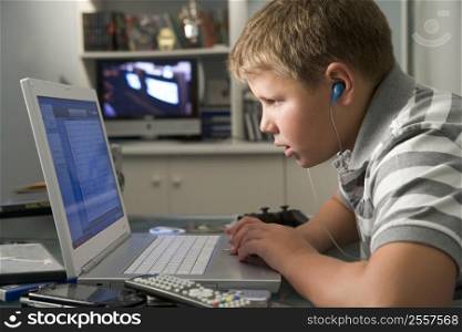 Young boy in bedroom using laptop and listening to MP3 player