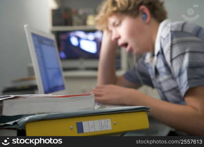 Young boy in bedroom yawning using laptop and listening to MP3 player