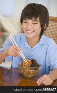 Young boy in dining room eating chinese food smiling