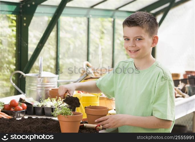 Young boy in greenhouse putting soil in pot smiling
