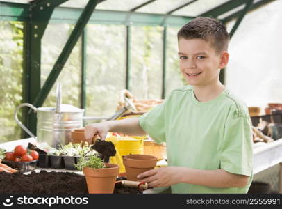 Young boy in greenhouse putting soil in pot smiling