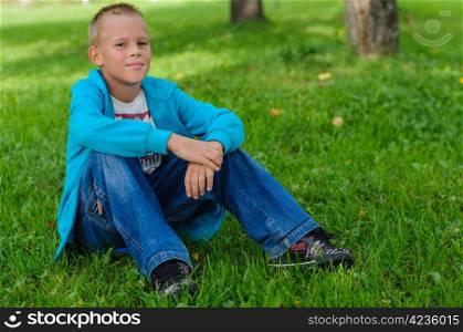 Young boy in jeans sitting on the grass