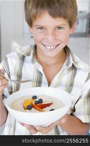 Young boy in kitchen eating oatmeal with fruit smiling