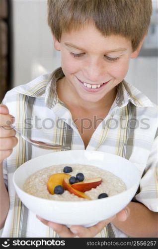 Young boy in kitchen eating oatmeal with fruit smiling