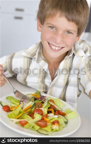 Young boy in kitchen eating salad smiling