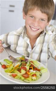 Young boy in kitchen eating salad smiling