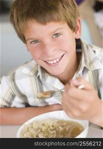 Young boy in kitchen eating soup and smiling