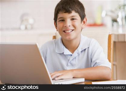 Young boy in kitchen with laptop and paperwork smiling
