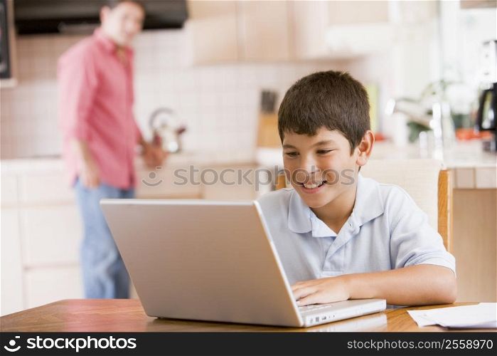 Young boy in kitchen with laptop and paperwork smiling with man in background