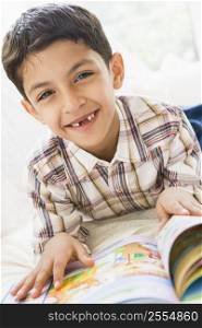 Young boy in living room reading a book and smiling (high key)