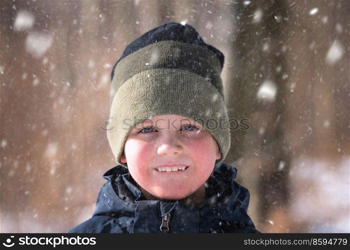 Young boy in the snow with a knitted hat and a cute smile on his face enjoying the outdoors