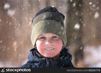 Young boy in the snow with a knitted hat and a cute smile on his face enjoying the outdoors
