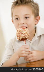 Young boy indoors eating candy apple