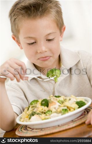 Young boy indoors eating pasta with brocolli