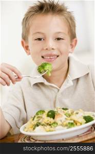 Young boy indoors eating pasta with brocolli smiling