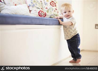 Young Boy Learning To Walk By Holding Onto Furniture