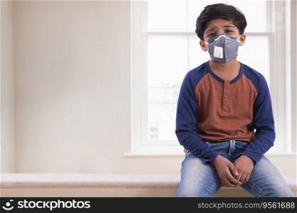 Young boy looking tired of wearing a pollution mask at home. (Children) 