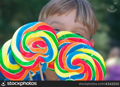young boy looks over the top of four huge lollipops. boy with lollipops