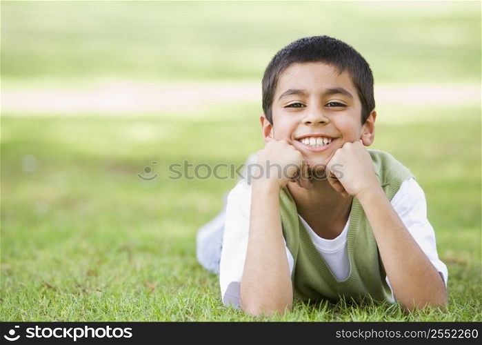 Young boy lying in grass outdoors in park smiling (selective focus)